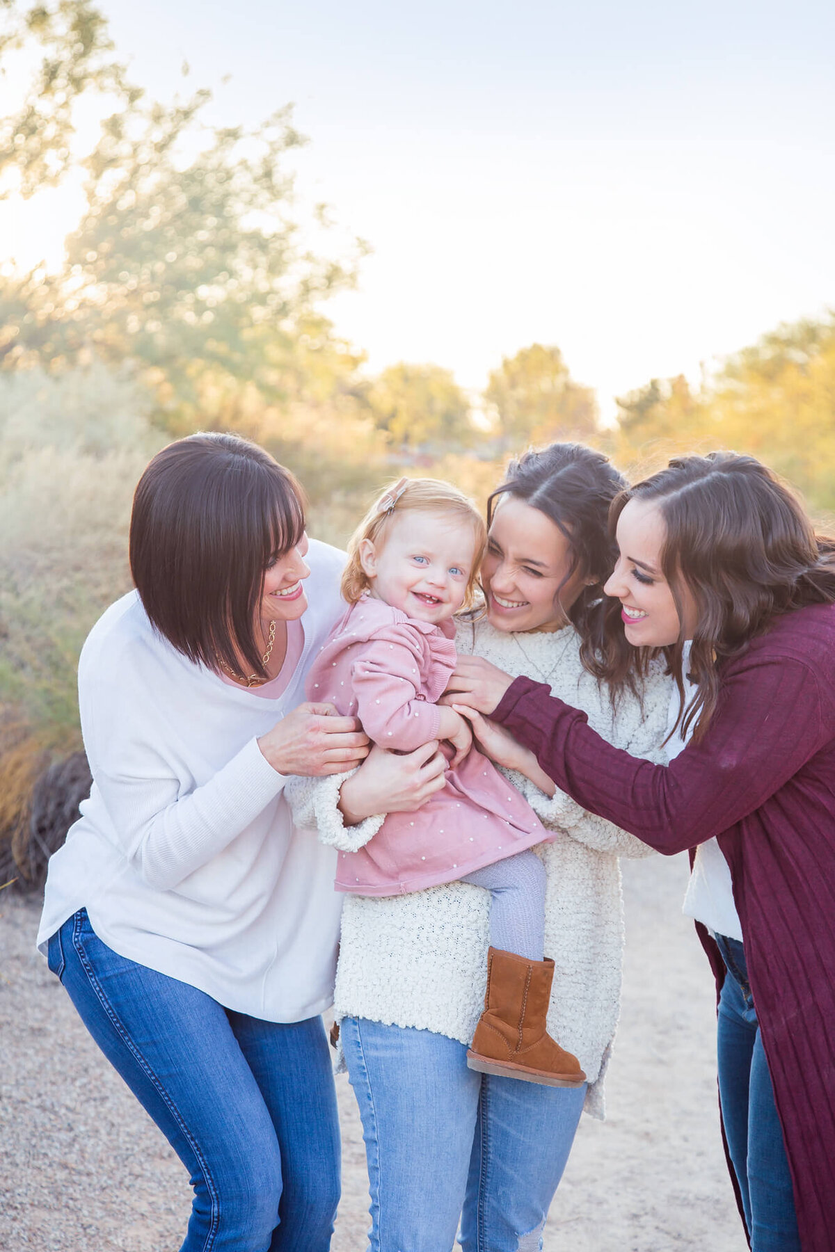 Happy toddler surrounded and tickled by mom , aunt, and grandma during desert family portrait sesison