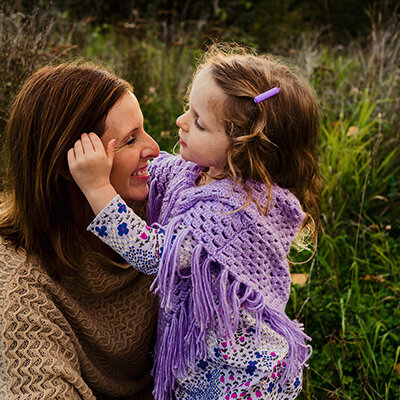Daughter sweeps back her mom's hair as they sit in a beautiful green field in Port Coquitlam, BC