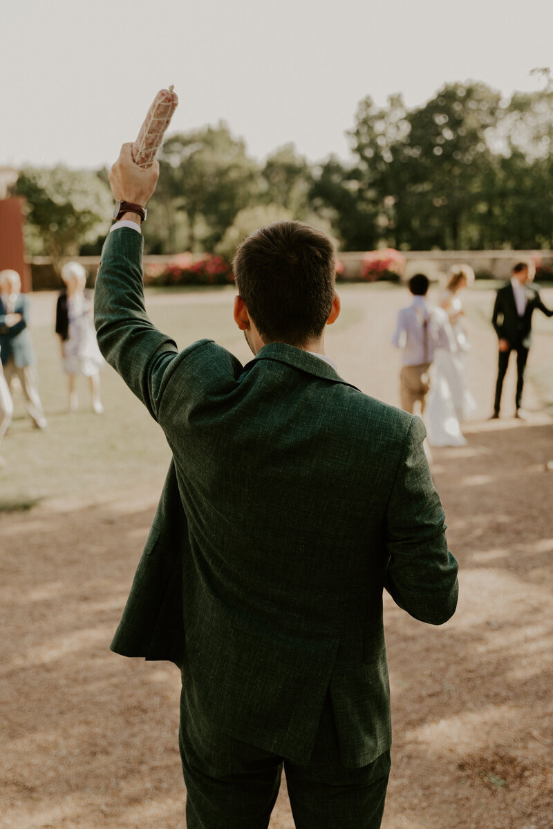 Marié brandissant un saucisson s'apprêtant à faire le lancer de saucisson. Immortalisé par Laura lors d'une séance photo mariage.