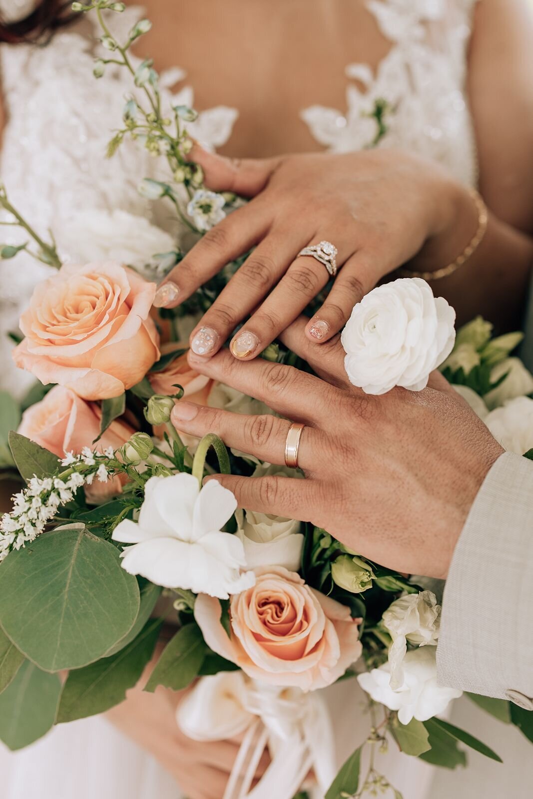 bride and grooms hands with their wedding rings on in front of a bouquet