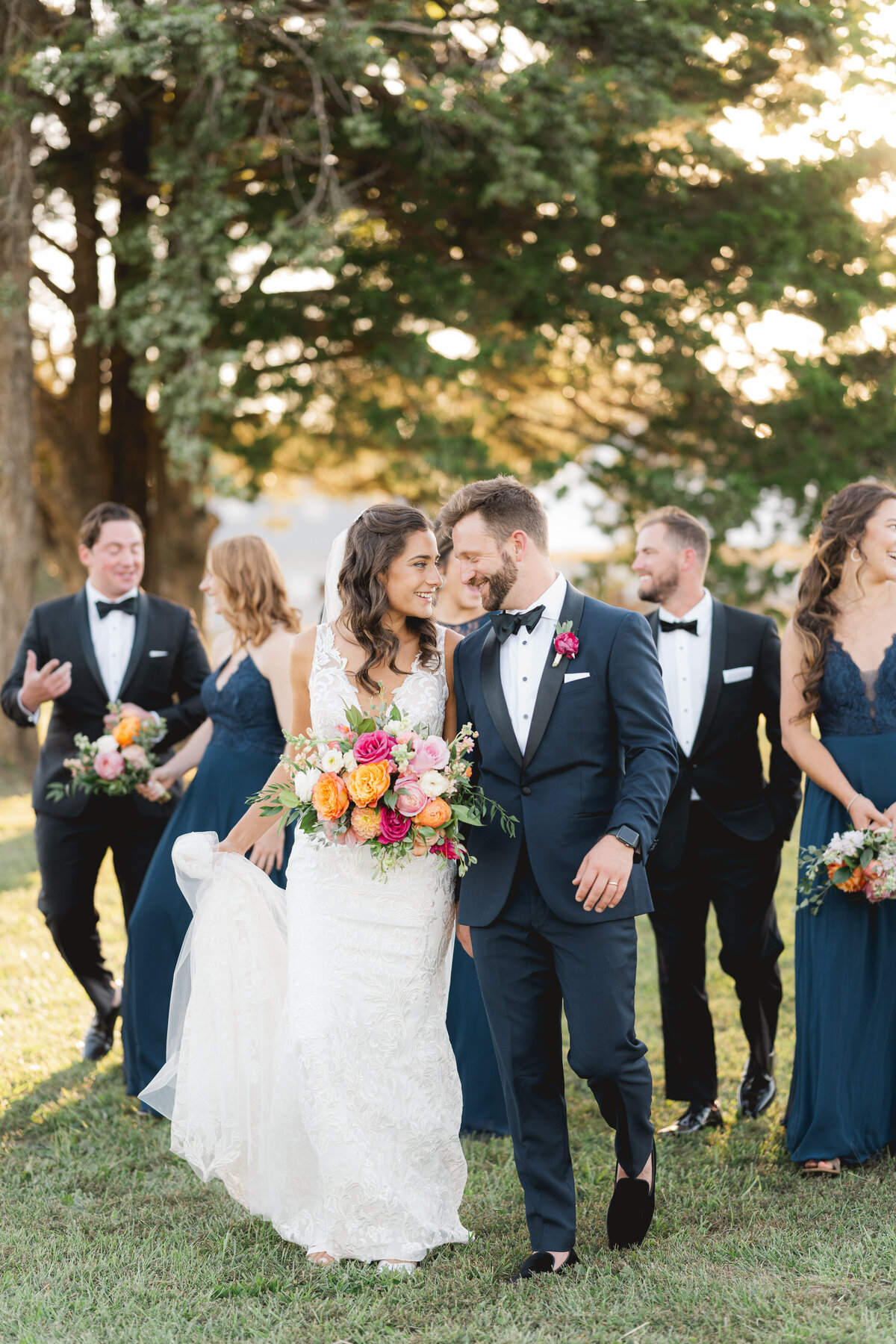 wedding couple in navy black tie with Pnina Tornei gown walking outside with wedding party behind them
