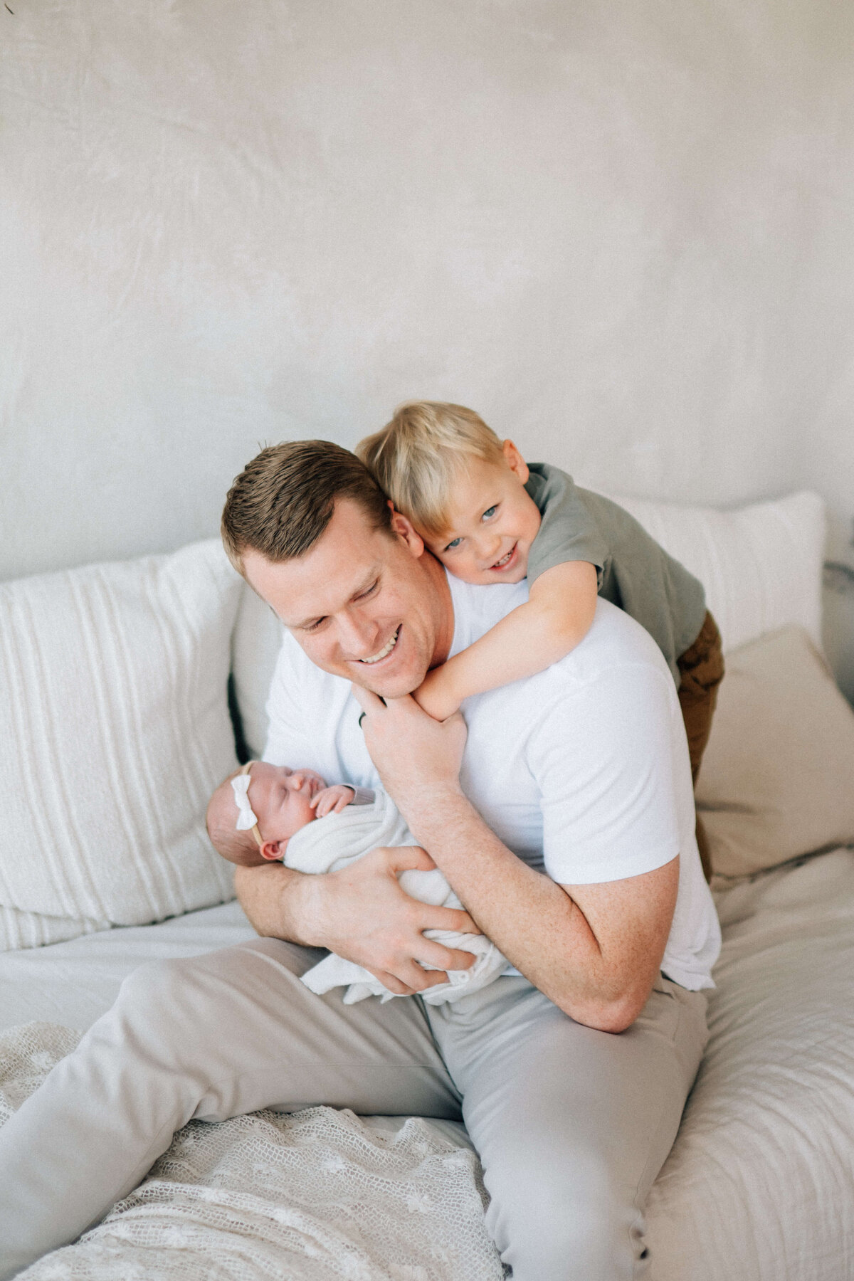 dad holding newborn baby while big brother hugs him from the back