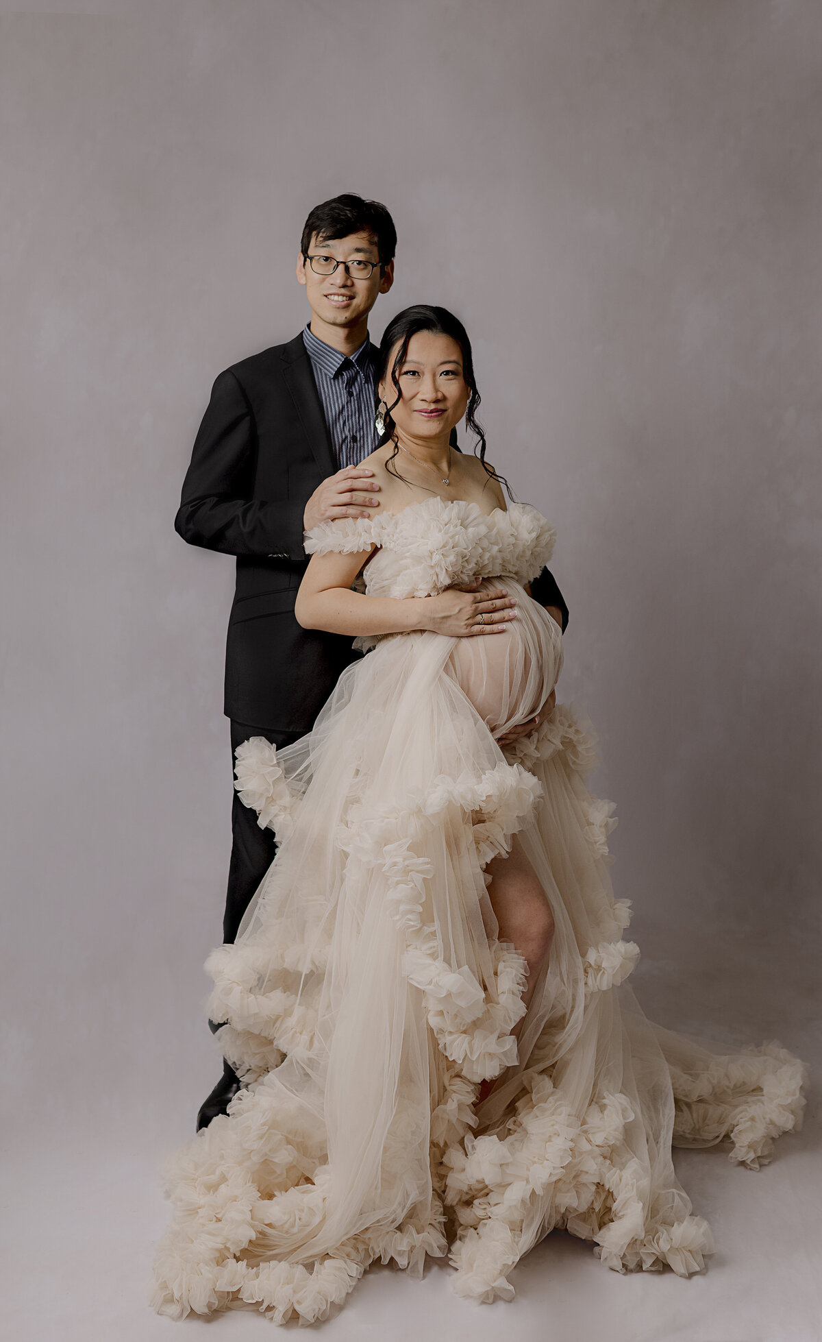 maternity session couple smiling at camera on white backdrop