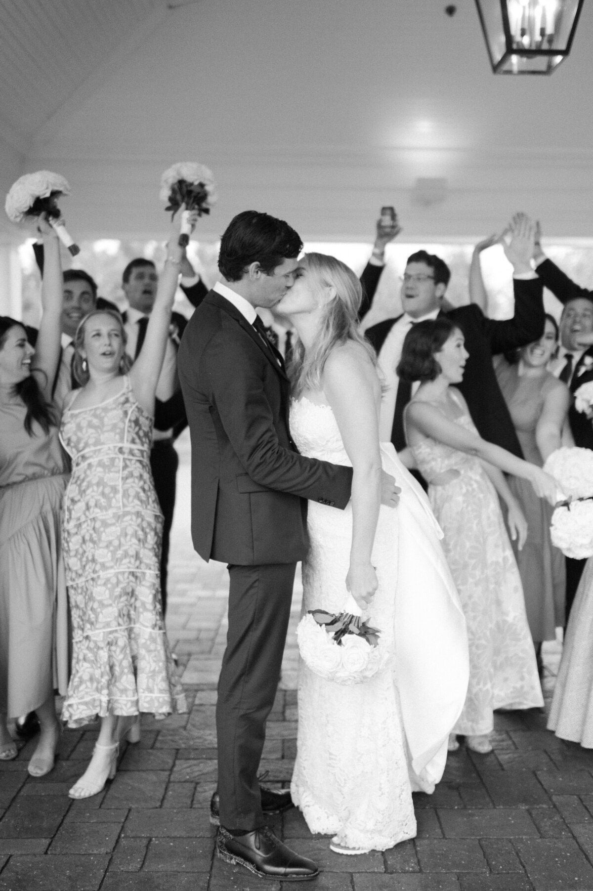 the bride and groom sharing a kiss under a covered outdoor area surrounded by friends and family