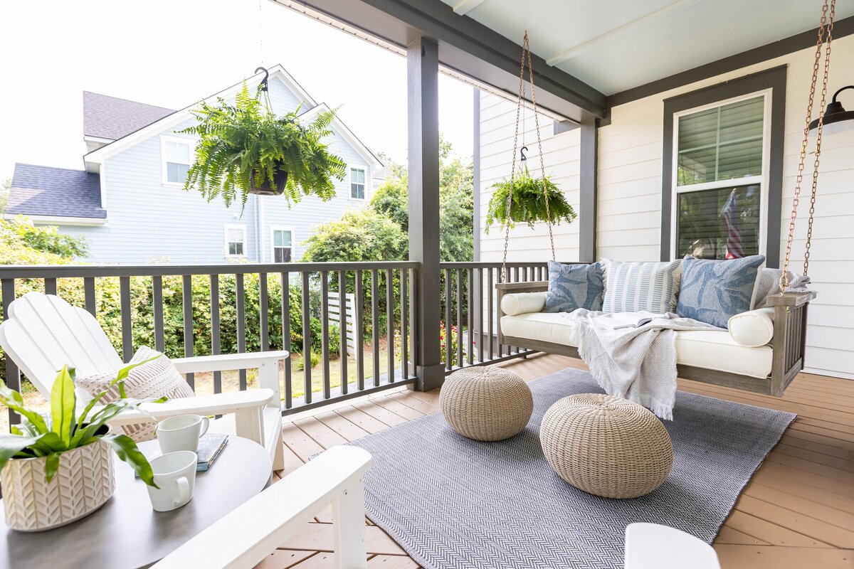 Charleston front porch with hanging ferns, white Adirondack chairs, and a cozy swing styled with blue pillows and woven ottomans – coastal-inspired outdoor design by KASL Design Co.