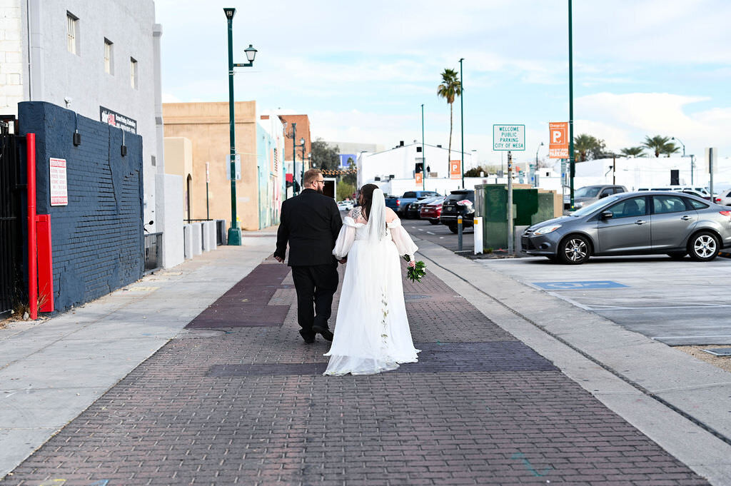 A wedding couple walking down an urban sidewalk.