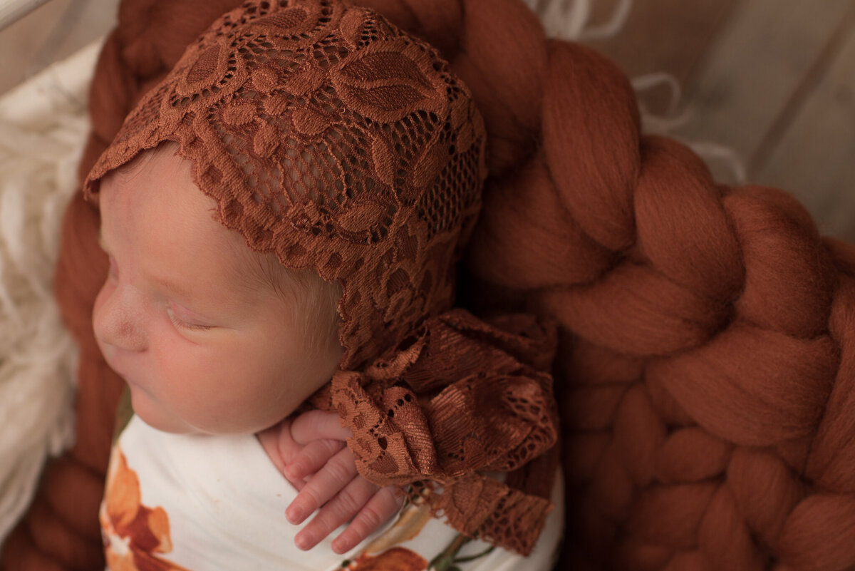 A side view of baby girl wearing orange bonnet with floral wrap in basket