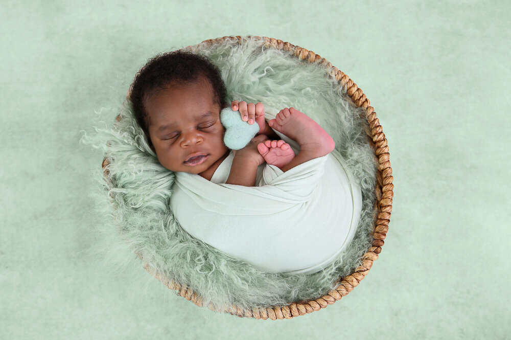 newborn boy holding a tiny heart on a mint background.