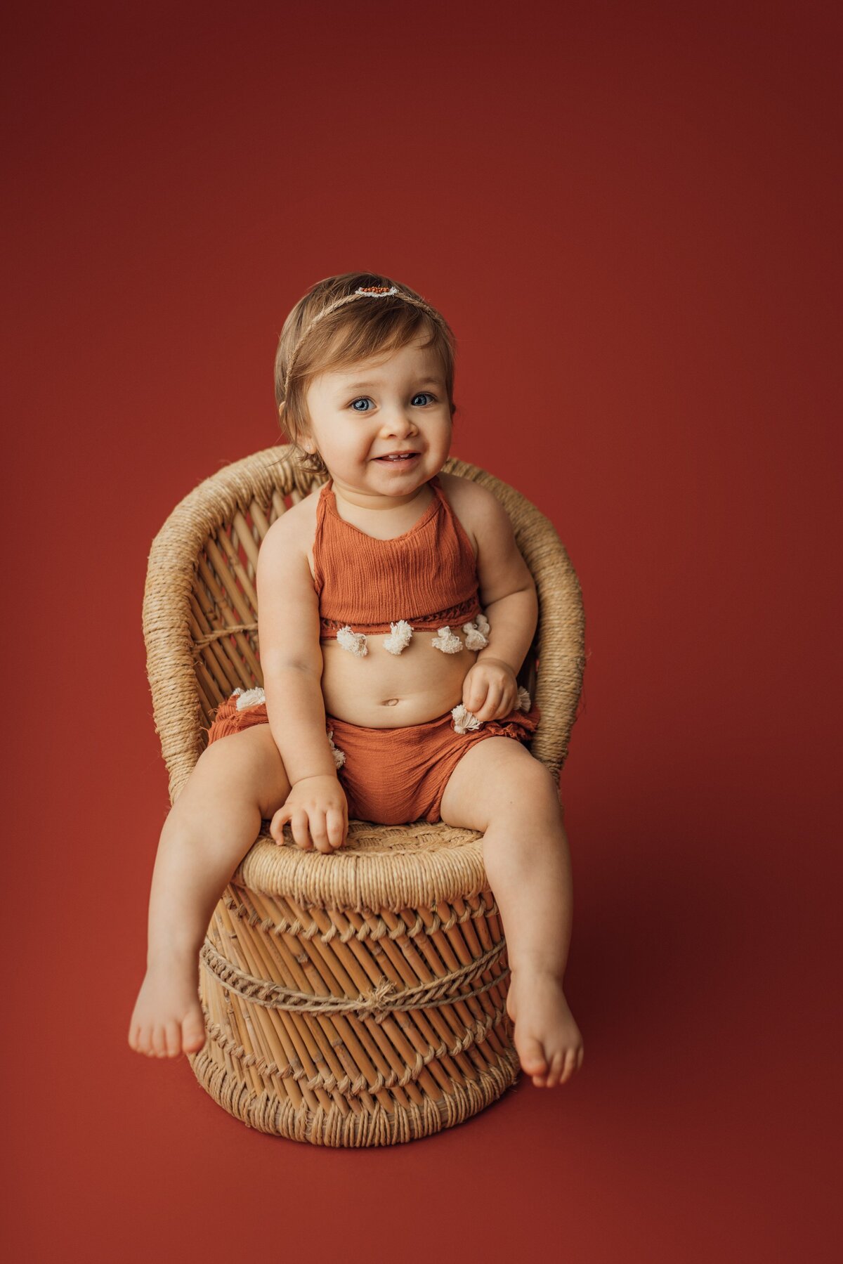 girl on rust sitting on rattan chair during first birthday photography session