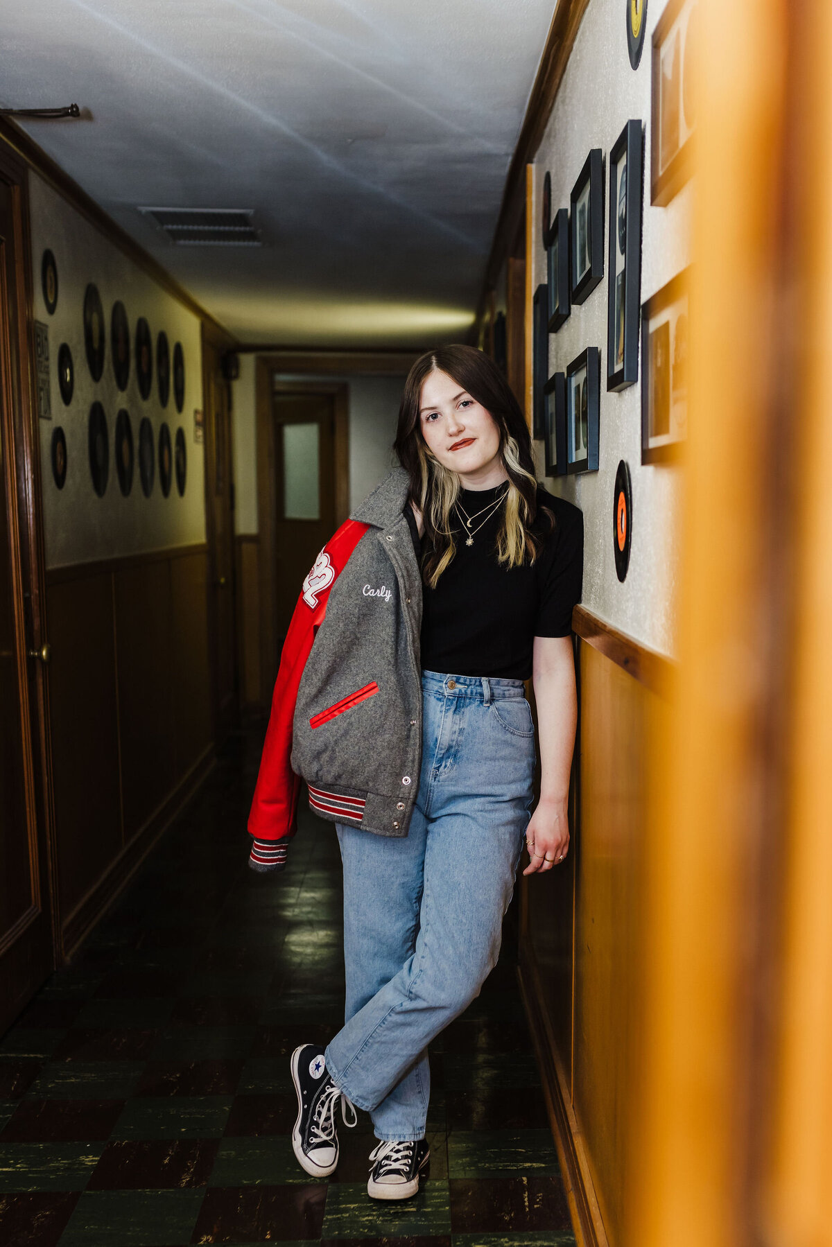 Senior portrait of girl with letterman jacket leaning on hallway wall in Gladewater Texas recording studio