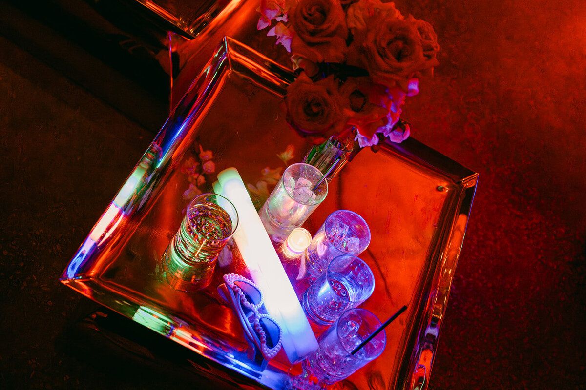 Late night flatlay of empty drink cups, an LED foam light, the brides sunglasses on table of the lounge in a luxury wedding reception