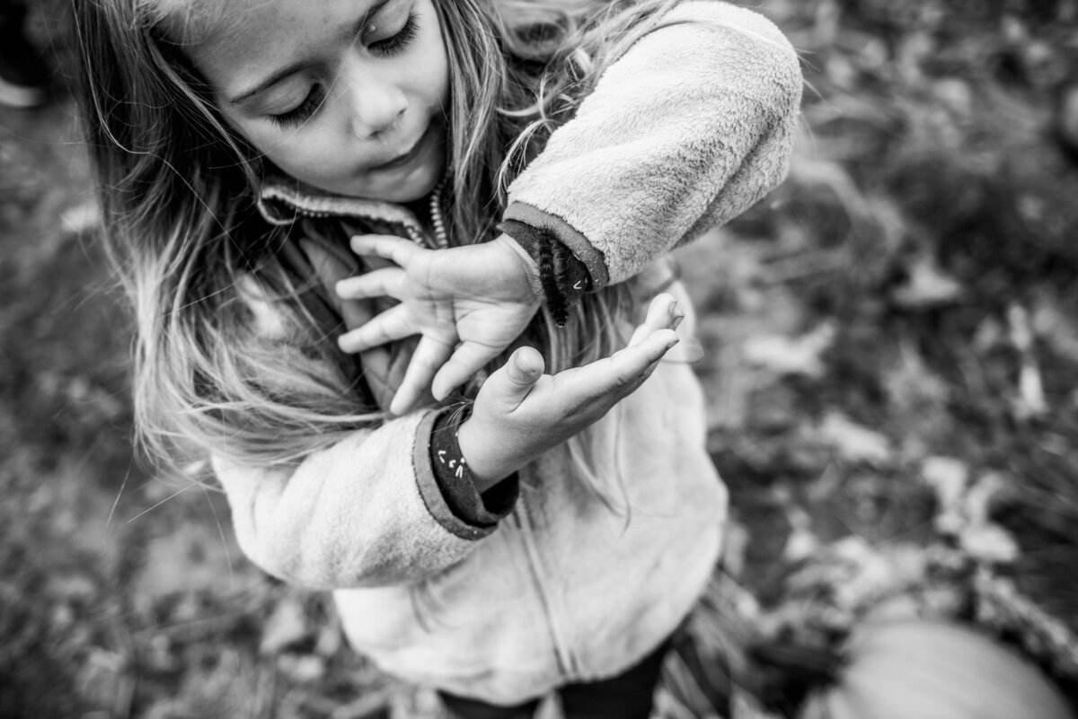 a little girl looks at a caterpillar on her arm