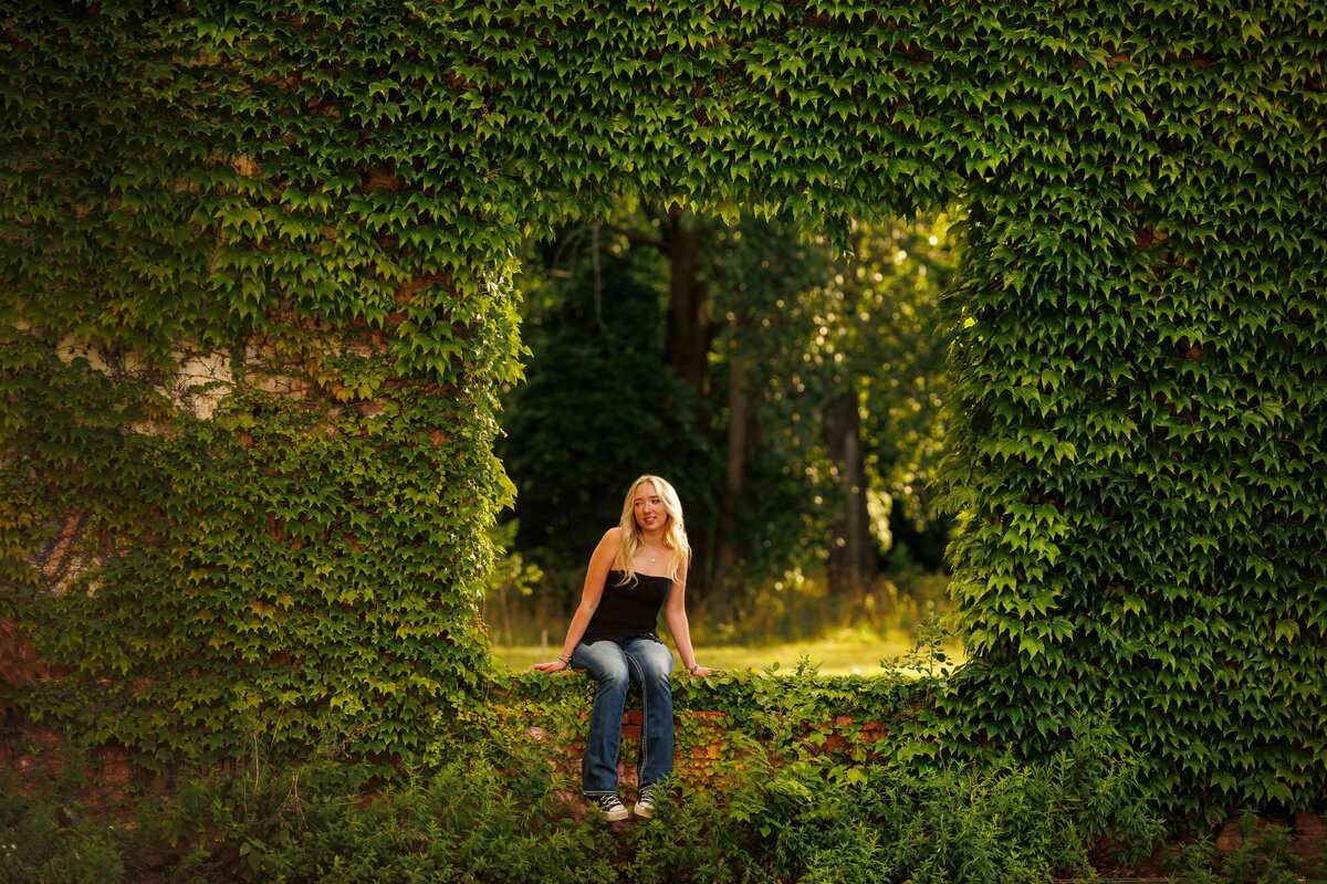 Maria is surrounded by green leaves on the brick wall.