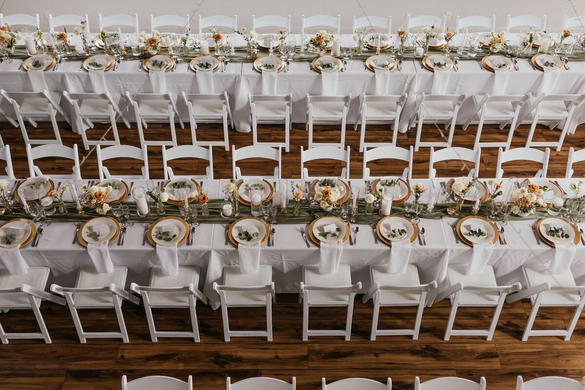 Overhead shot of indoor dining tables with place settings and floral arrangements at a wedding reception.