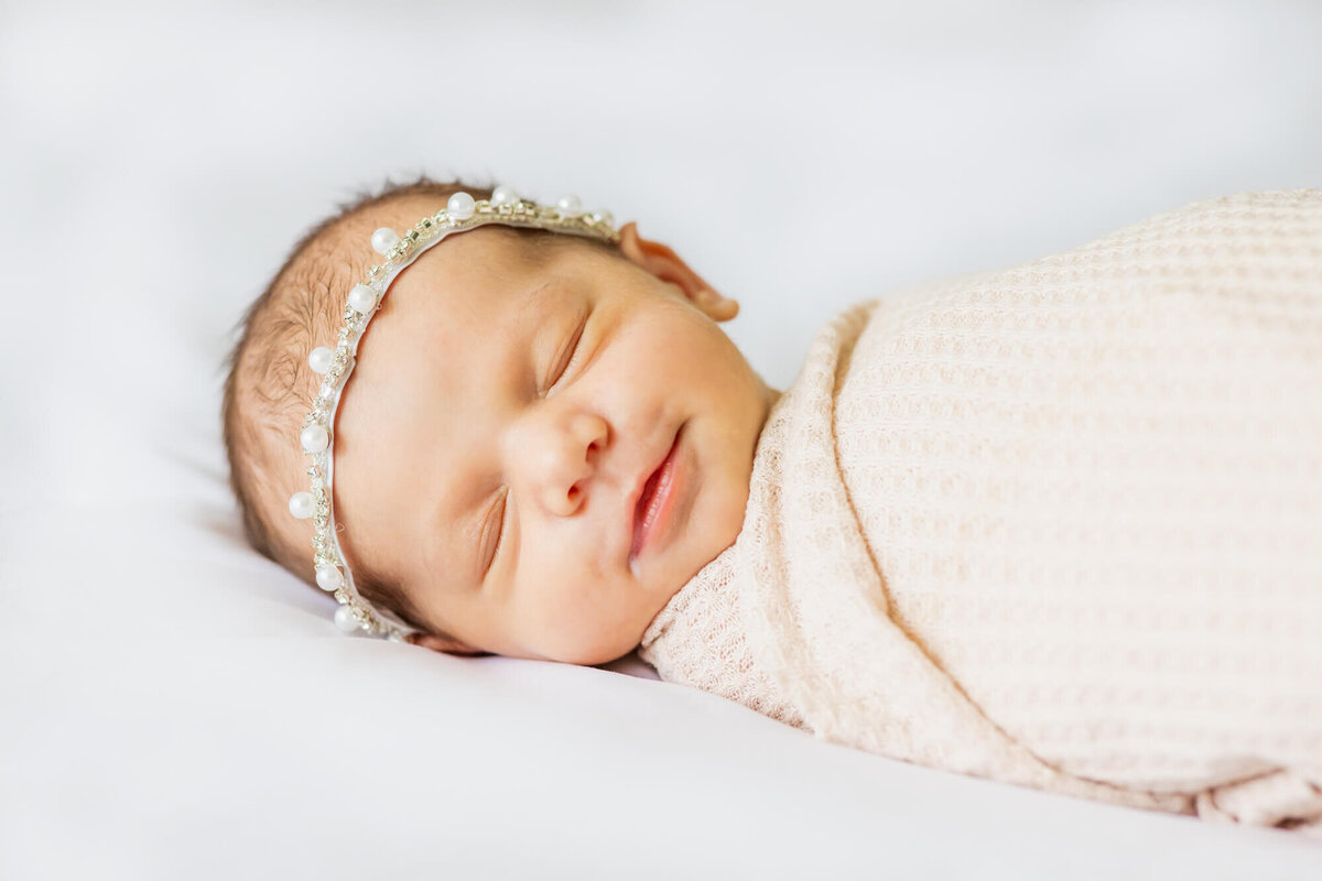 Newborn baby girl laying on a bed smiling