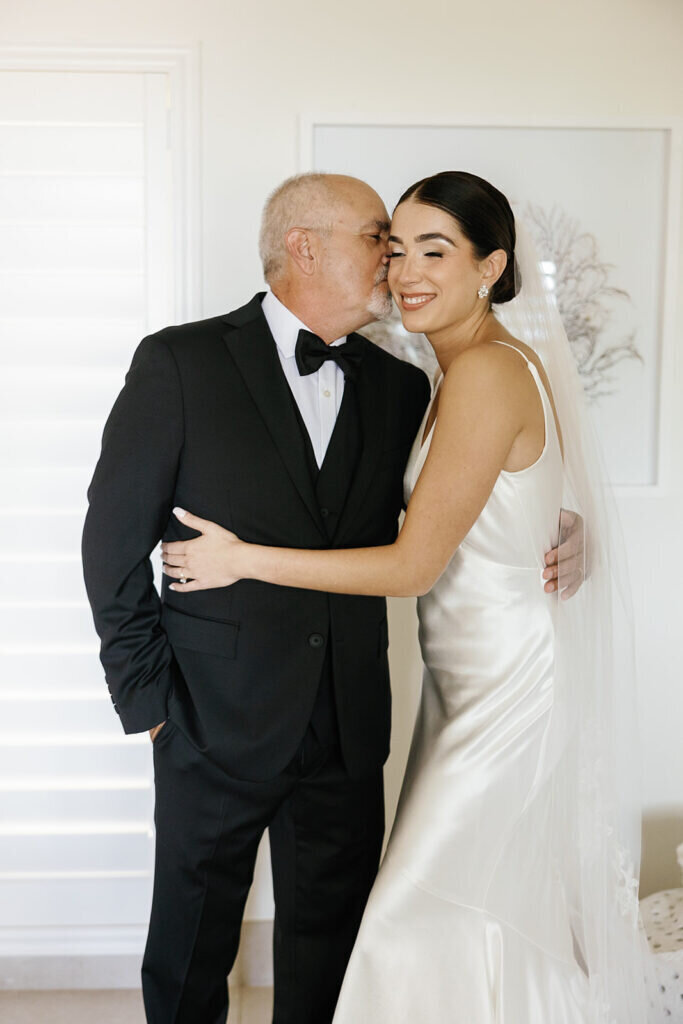 A touching moment as the bride's father kisses her forehead, showing deep love and emotion on her wedding day. Captured by Claudia Amalia Photography, a destination wedding photographer in the Florida Keys.
