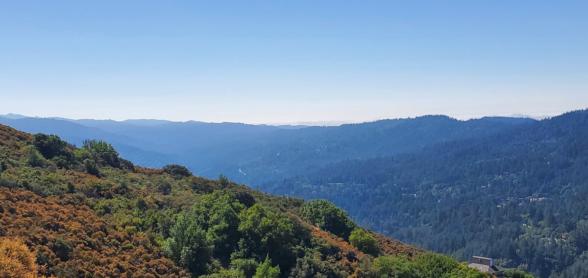 Green mountains in the foreground with the shadow of blue mountains stretching under a blue sky.