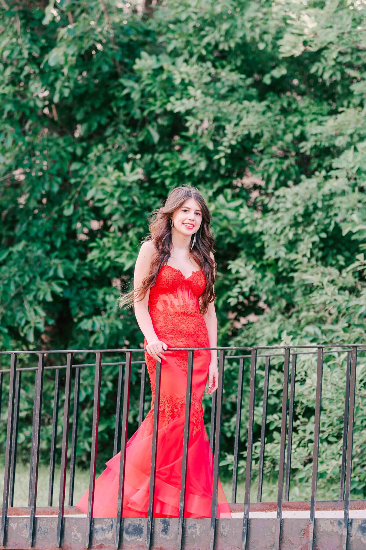 A young girl in a red dress standing  by a black railing