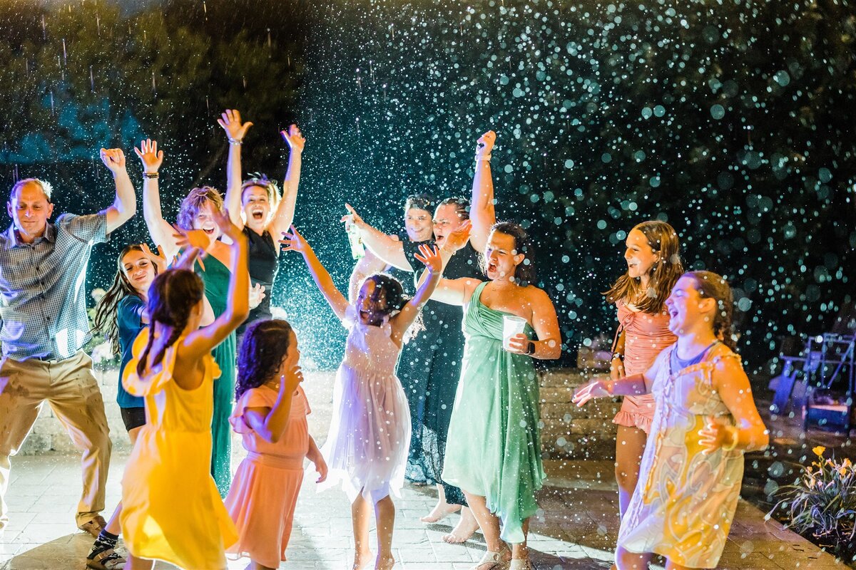 guests dressed in colorful clothing dancing in the rain on the stone patio at Willowbrook Wedding venue