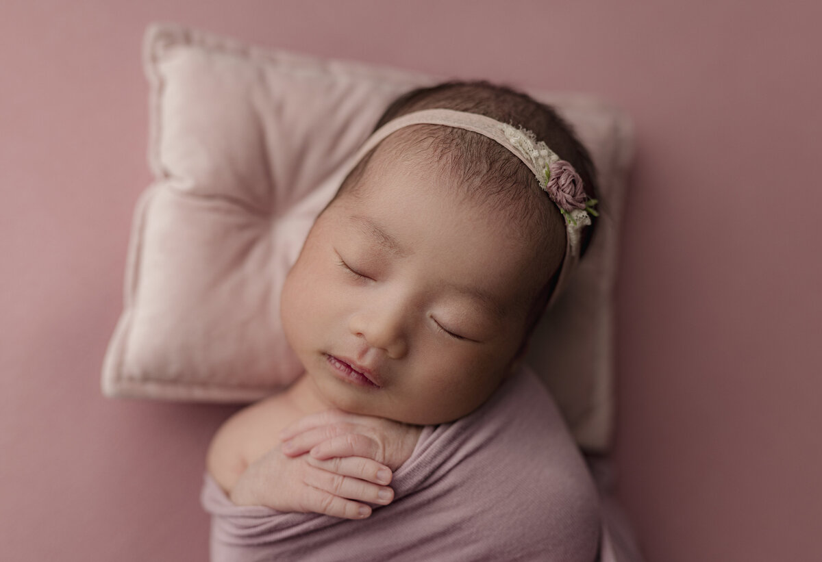 baby laying on pink backdrop wearing pink flower headband