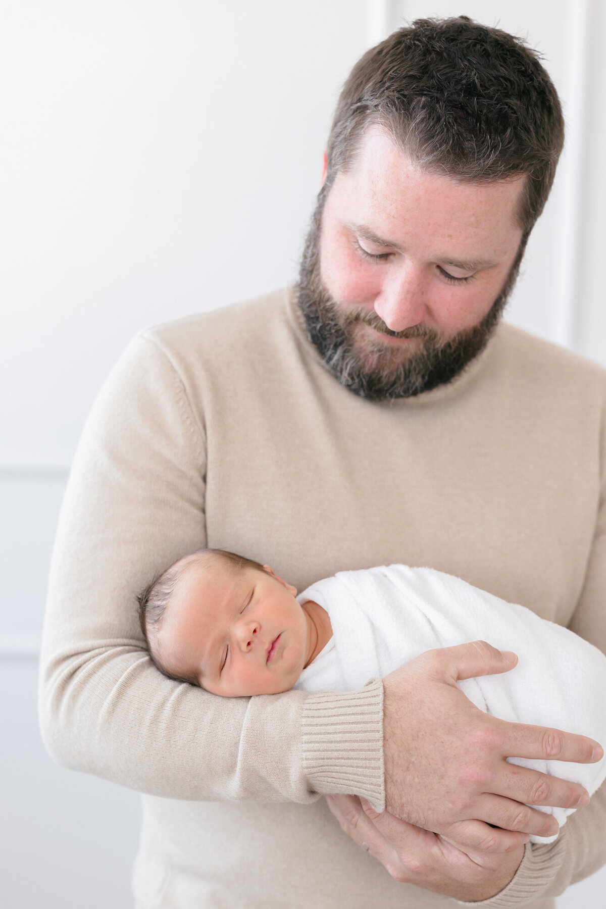Dad holding his sleeping newborn wrapped in a white swaddle taken by a louisville newborn photographer