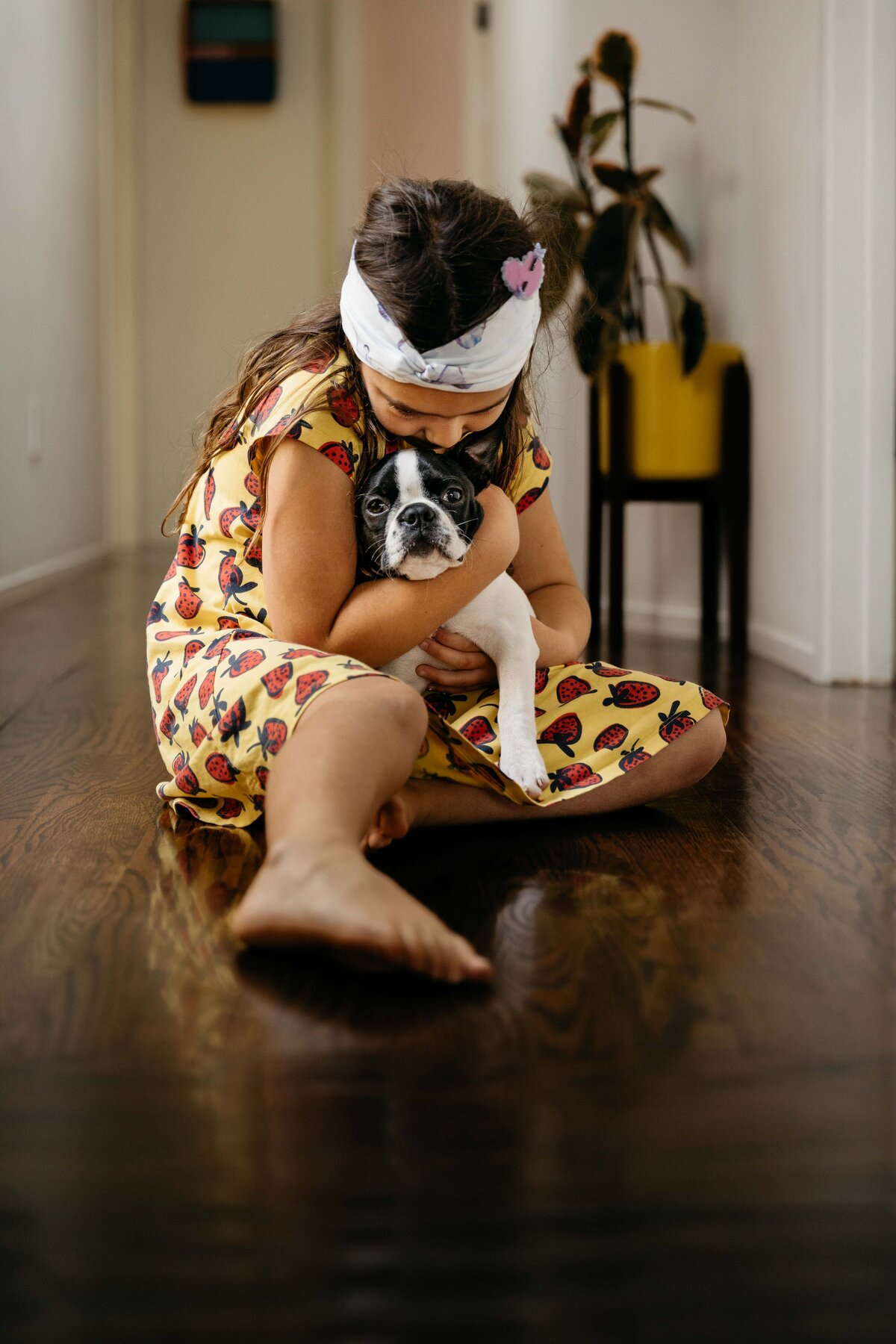 Young girl snuggling with her Boston terrier puppy at home.