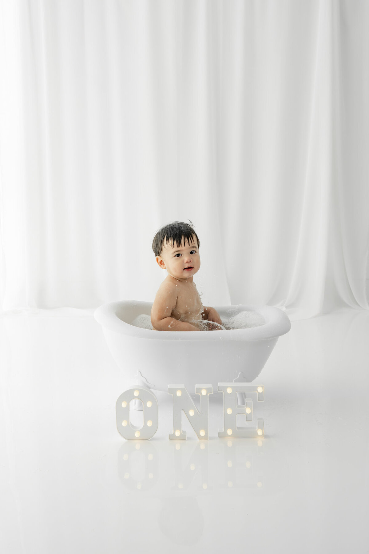 Boy in bubble bath during themed cake smash session— captured by Alliston and Barrie cake smash photographer.