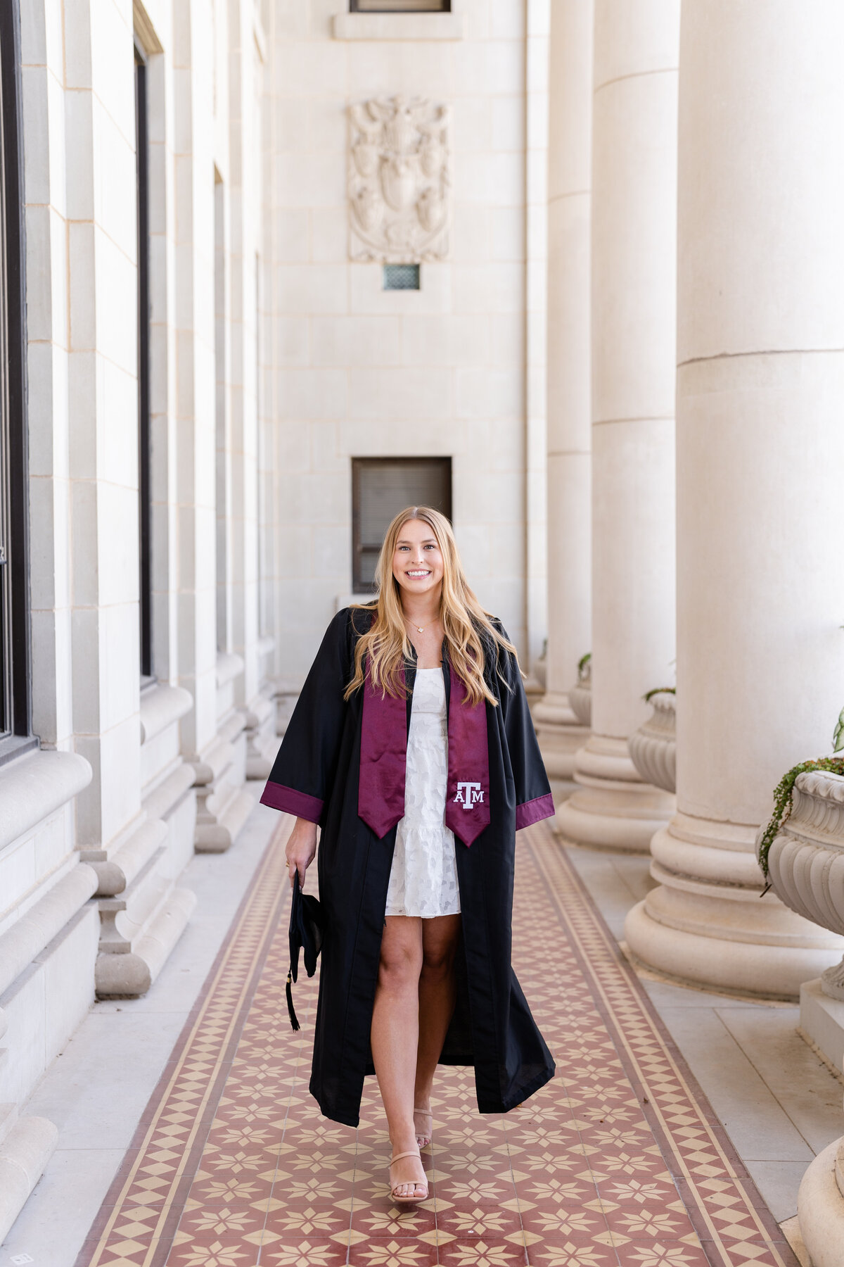 Texas A&M senior girl walking and wearing gown and stole while holding cap and laughing in the columns of the Administration Building