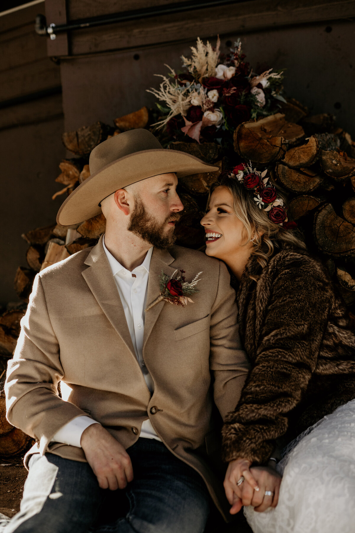 Bride and groom sitting together in front of a pile of logs