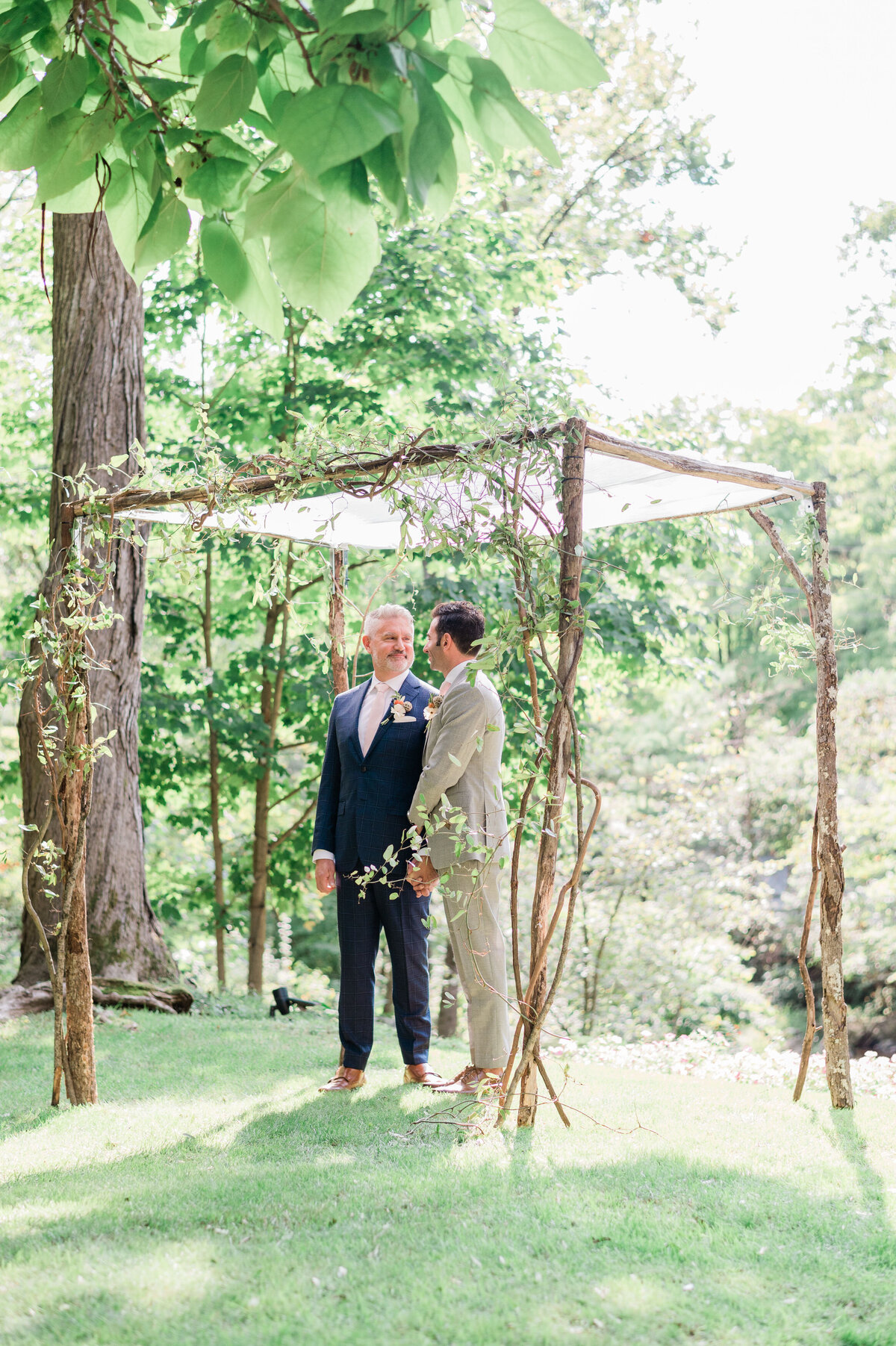 Grooms stand underneath their wedding arch before the ceremony begins 