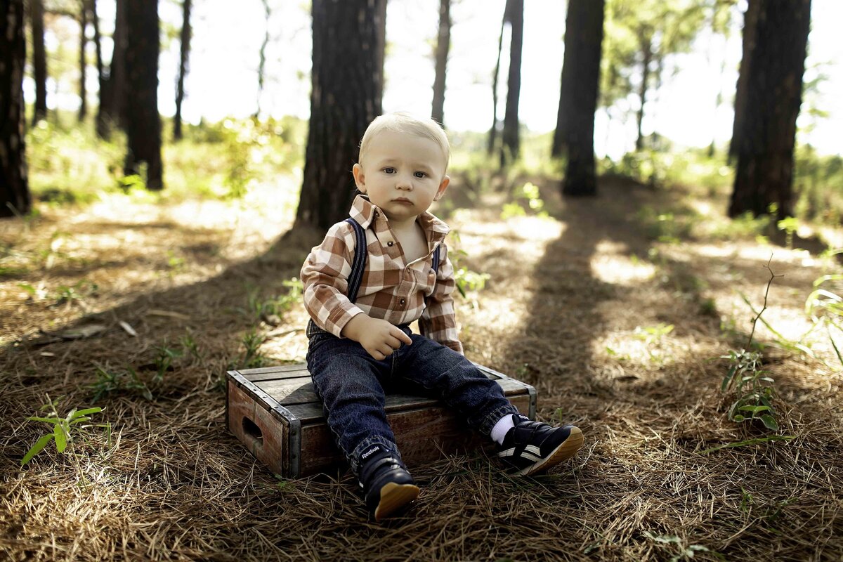 Birthday boy with suspenders, playfully standing under the shade of pine trees with a joyful expression
