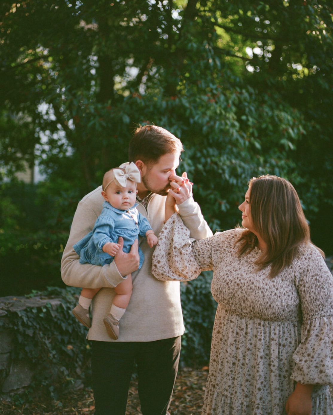 Couple holds hands sharing kiss while holding baby surrounded by greenery by huntsville alabama photographers