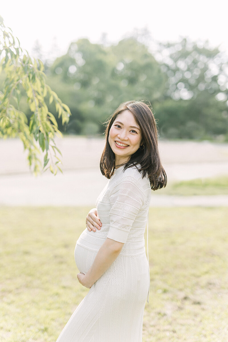 横浜市で撮影。桜の葉のそばで、おなかに両手を添えて笑顔を見せる妊婦さんのおしゃれなマタニティフォト