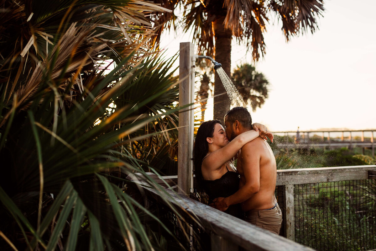 married couple kisses under beach shower in St. Andrews State Park -after intimate sunrise session with Panama City Beach photographer Brittney Stanley of Be Seen Photos