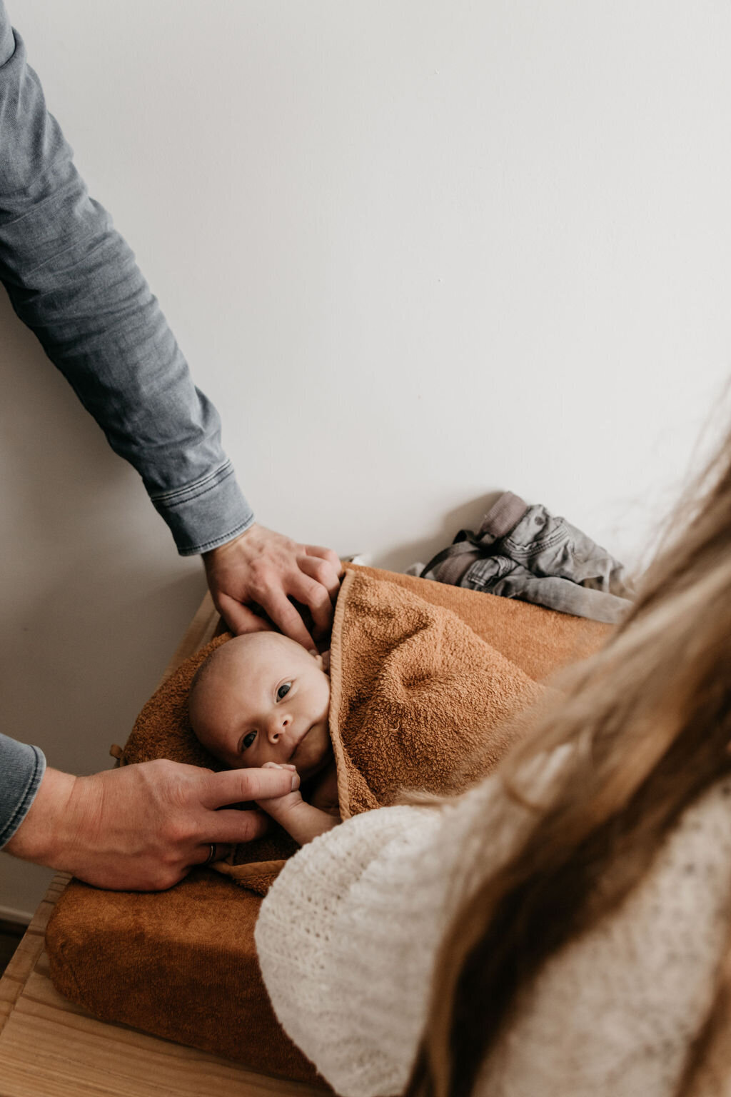 Newborn baby wordt aangekleed door moeder en heeft hand vader vast tijdens newbornshoot