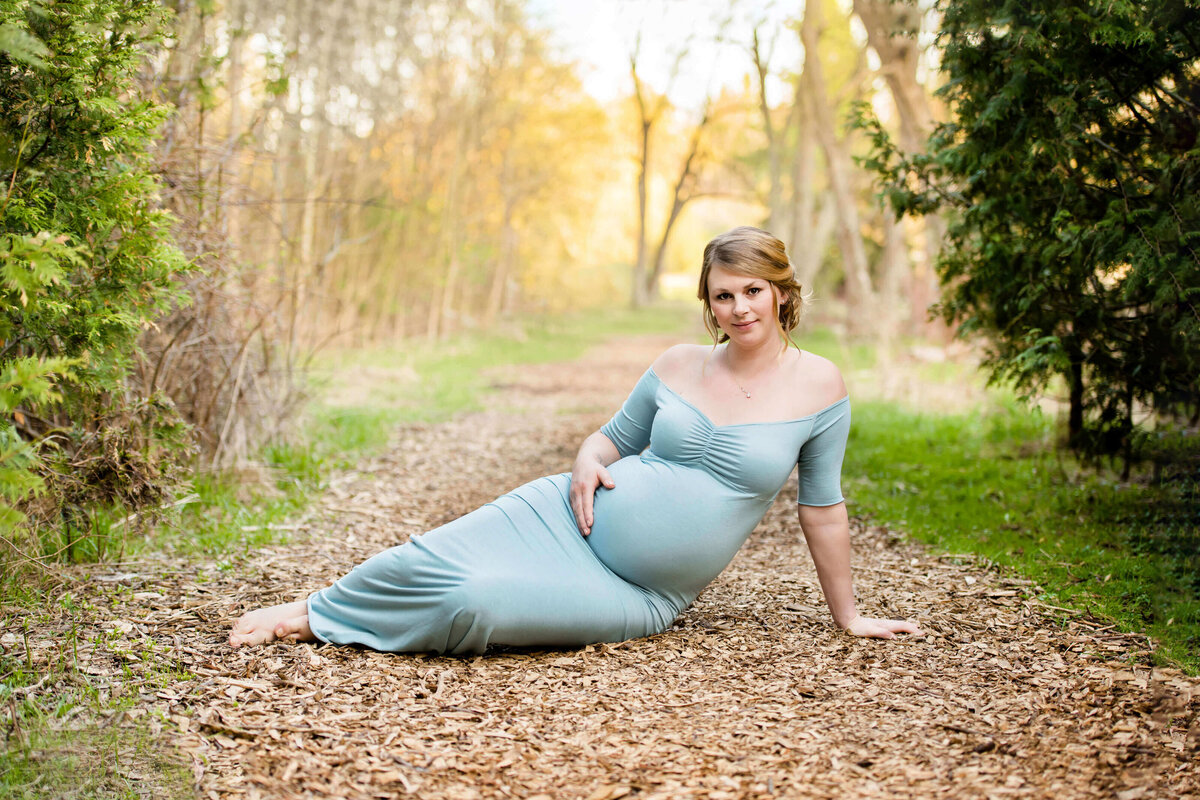 pregnant woman sitting on the ground wearing a blue maternity dress for her outdoor maternity photos