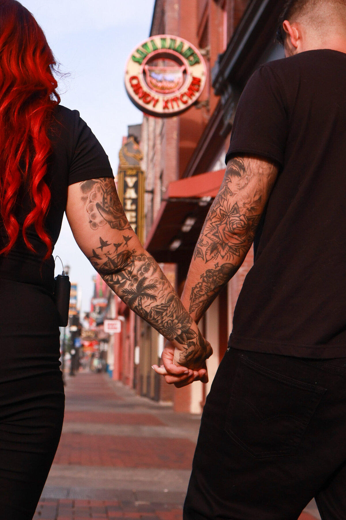 man and womanwith tattooes holding hands on brick walk path with signs in the background