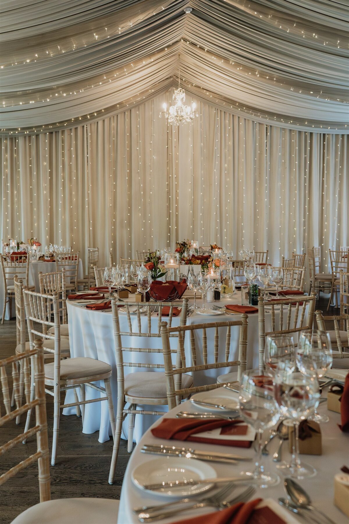 A wide photograph of five large circular tables in the ballroom of Logie Country House. The tables are set for a wedding meal and fairy lights can be seen above. A small chandelier hangs from the ceiling.