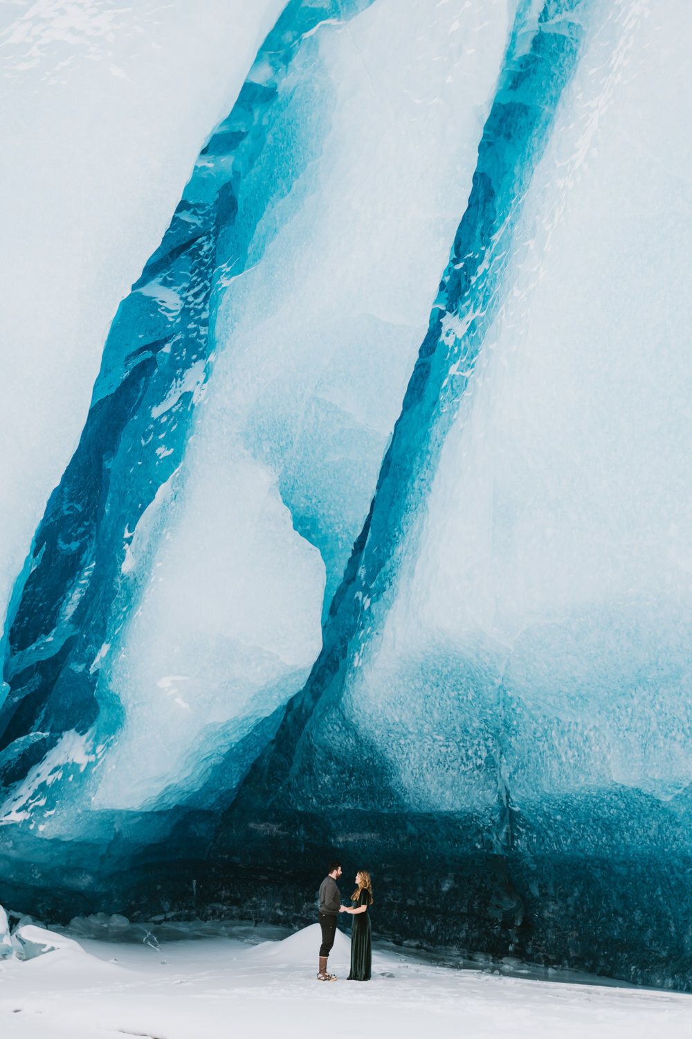 a couple sharing their vows in front of a blue glacier wall on their helicopter elopement day