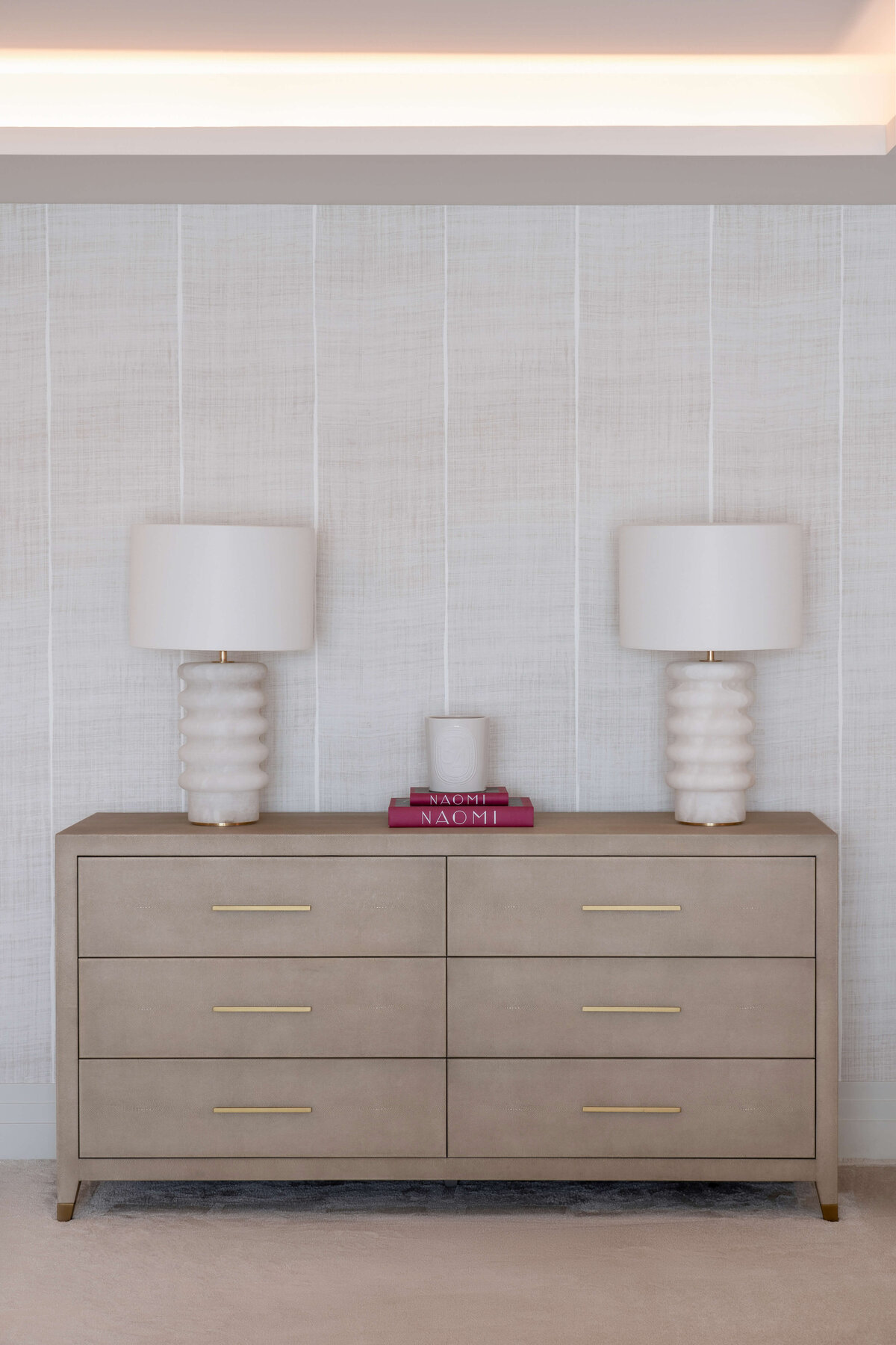 A light neutral dresser in the primary bedroom. Atop the dresser are two large chic white lamps.