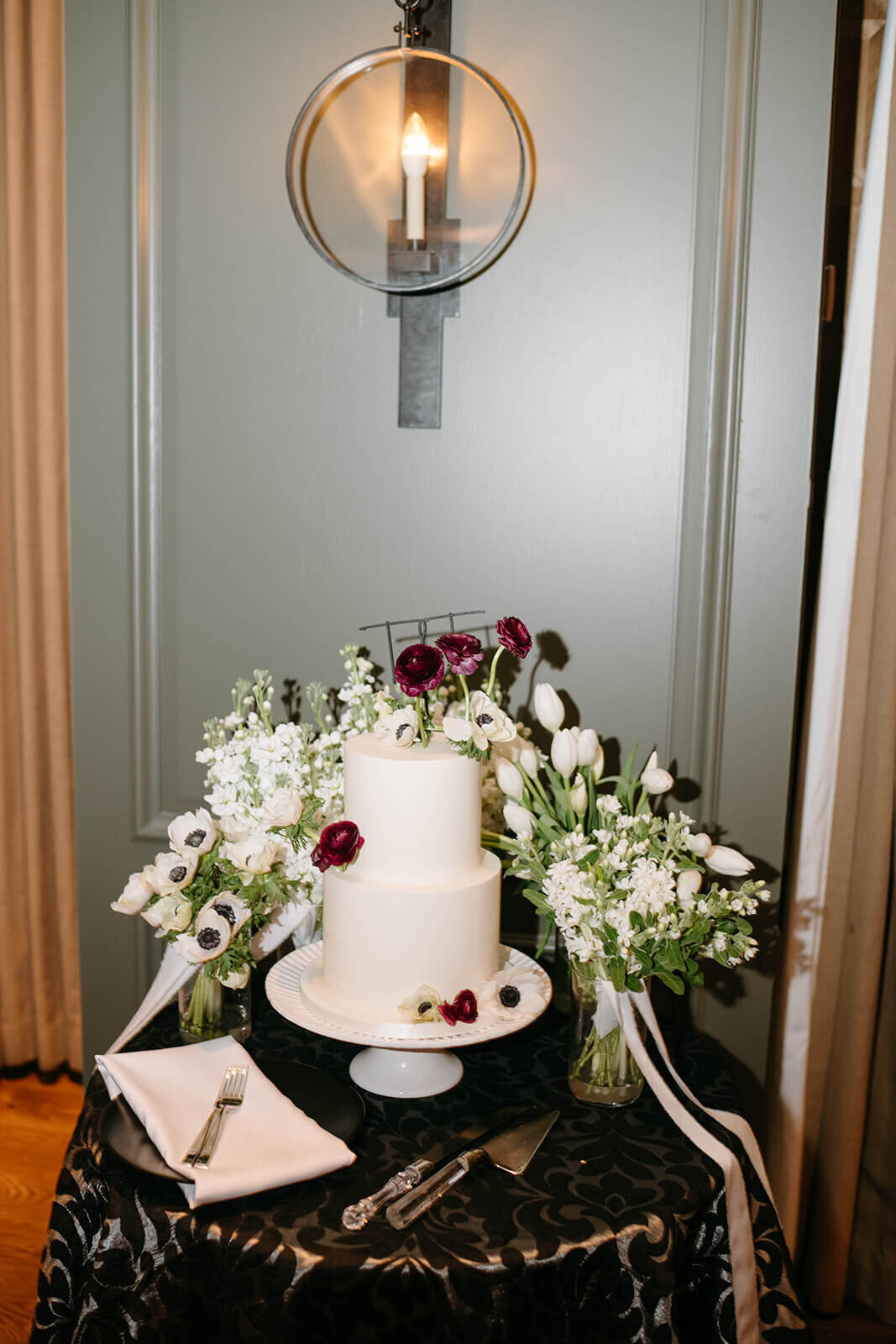 Beautifully simple wedding cake surrounded by bouquets of flowers and accented by colorful flower blooms resting upon a cake table at the St. Regis wedding reception.