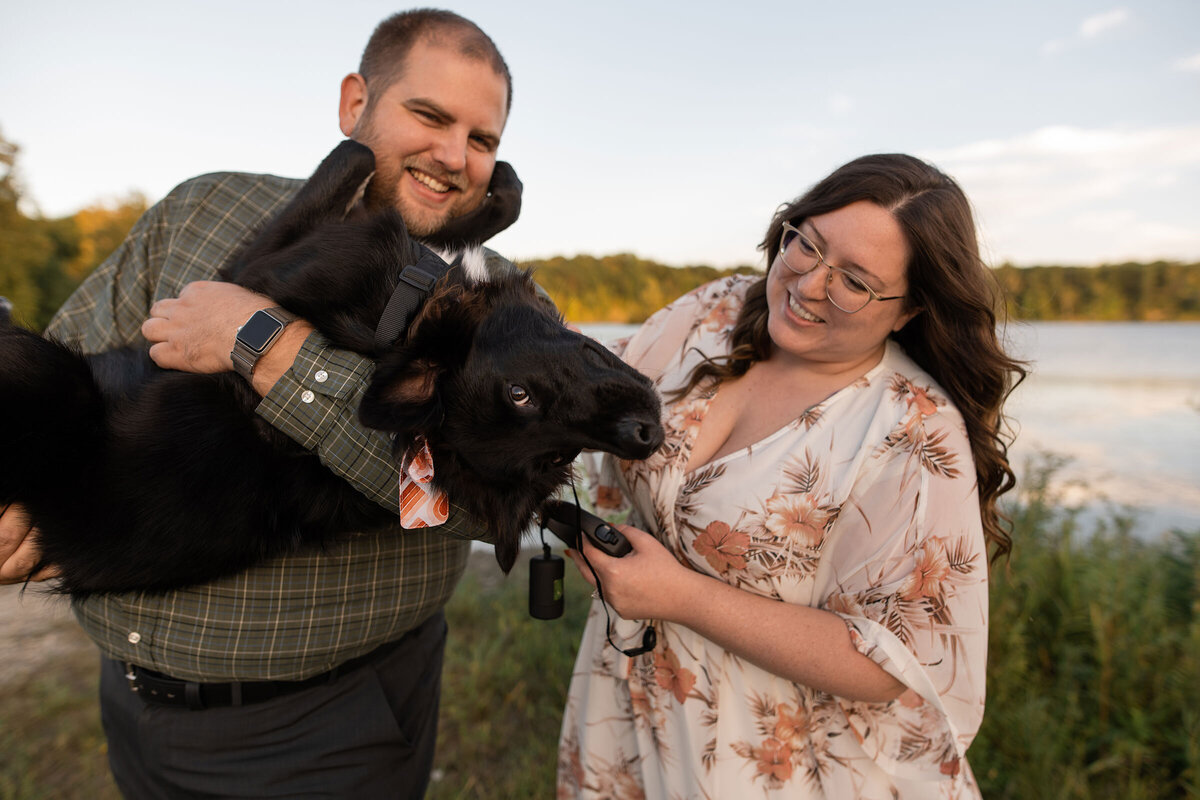 Couple laughs while holding and petting black puppy