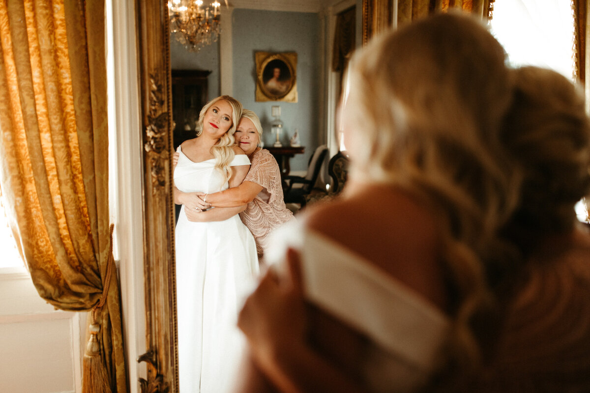 Bride and her mother hugging and getting emotional while looking in the mirror after bride put on her wedding dress