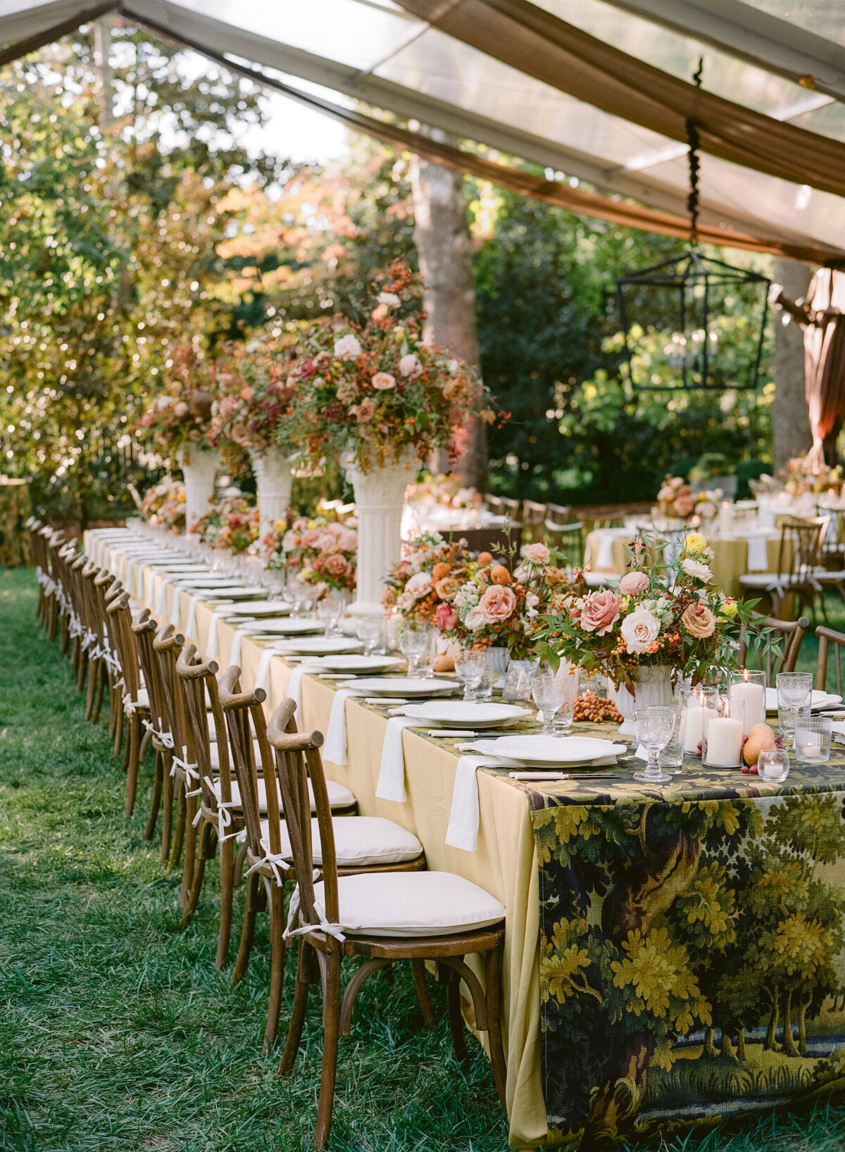 Lush fall florals for low and high centerpieces at fall wedding reception. Clear tented wedding reception in the family's back yard creating an intimate wedding reception environment. Whimsical and organic floral design in colors of copper, yellow, blush,and brown. Fall florals with sweet peas, dahlias, butterfly ranunculus, roses, mums, and bittersweet berries. Design by Rosemary & Finch Floral Design in Nashville, TN.