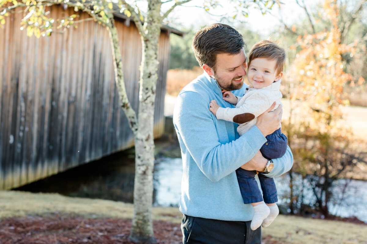 Dad looks at young son as they stand in front of old covered bridge in Roswell