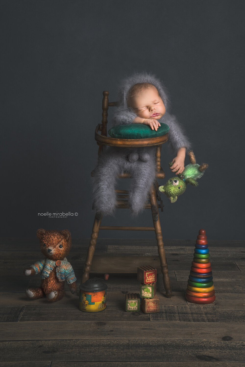 Newbornbaby sleeping in highchair surrounded by vintage toys and bears.
