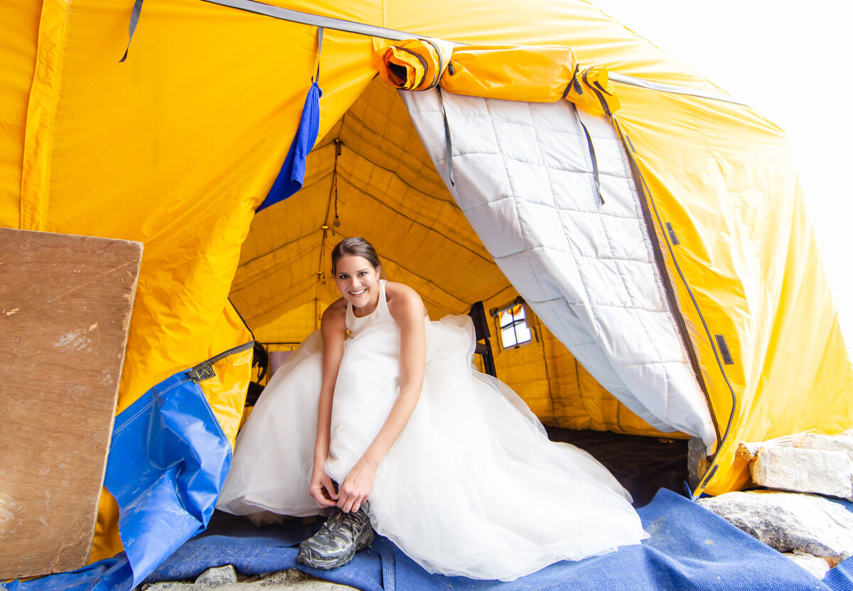 The adventurous bride puts on her hiking boots in the entrance to a food tent after her wedding gown  formations of the Khumbu Icefall at Everest Base Camp in Nepal
