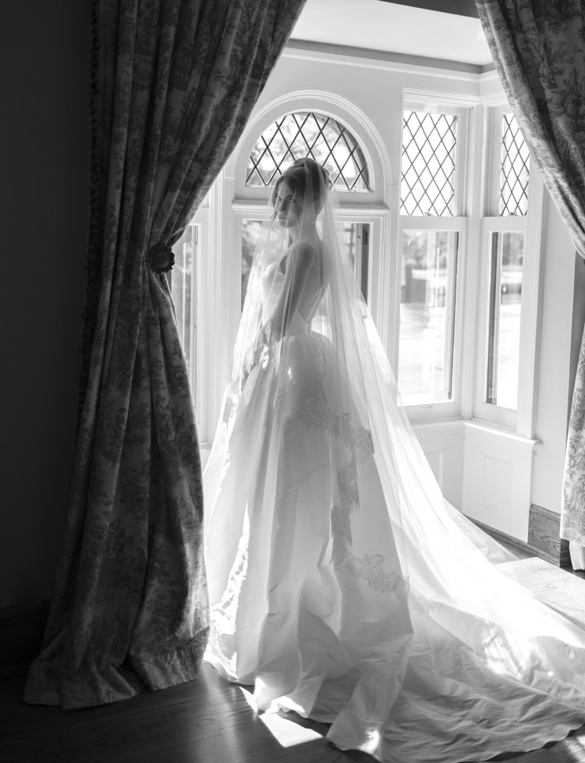 a bride in a stunning ballgown gazes at the camera from near a window, taken in a unique wedding getting ready venue in Detroit, Michigan