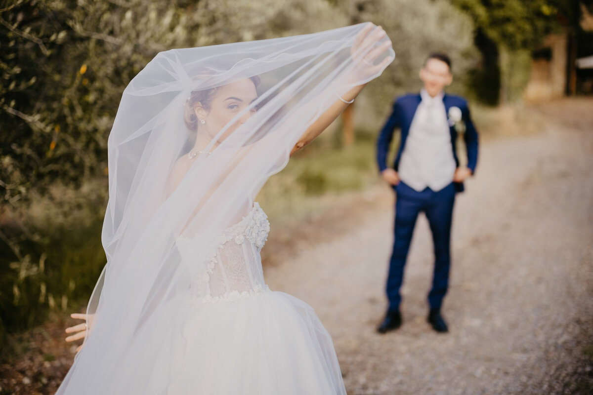 Bride playing with veil in front of smiling groom, Castello il Palagio Chianti wedding photographer Tuscany.