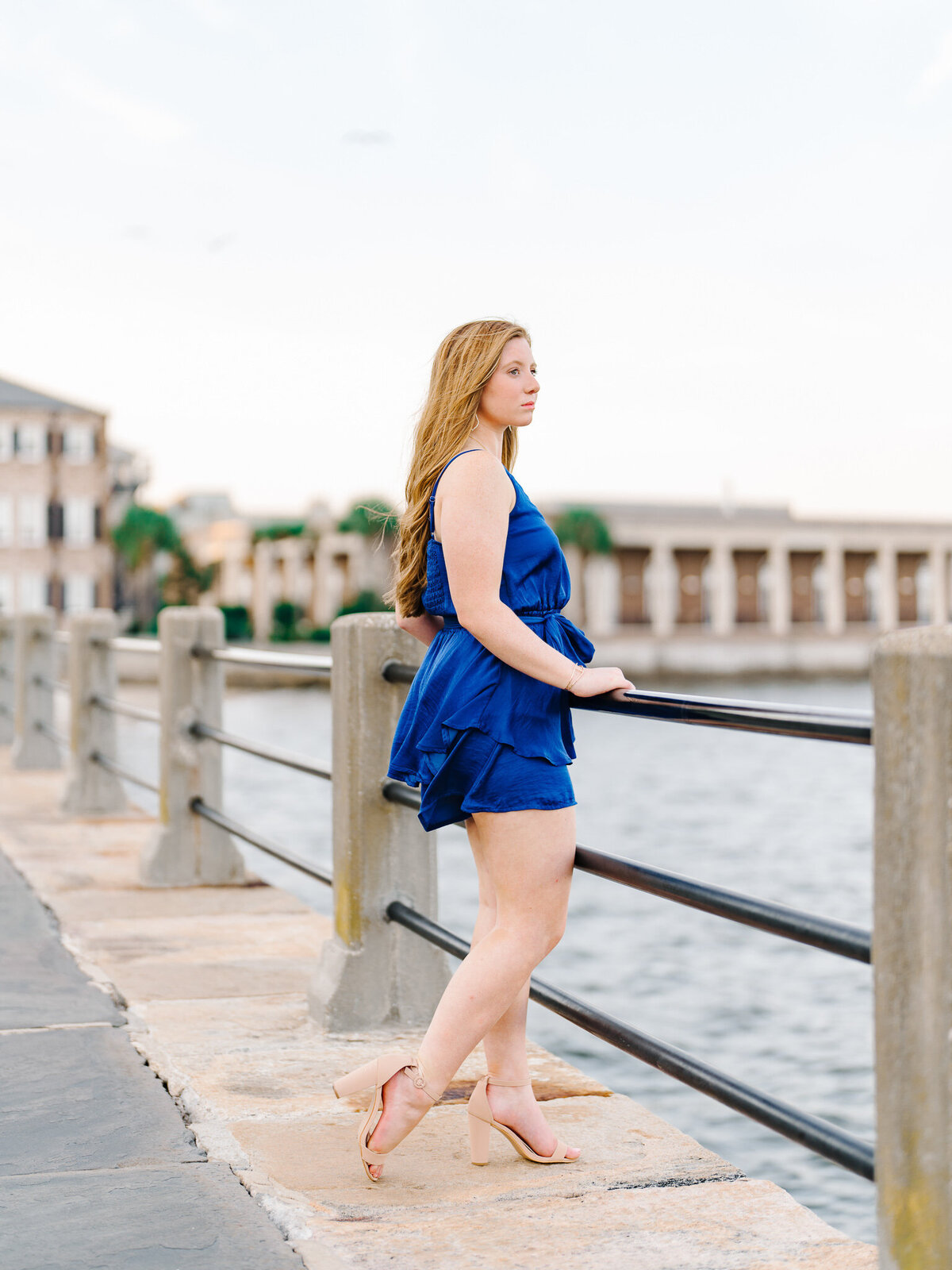 Teen girl in blue dress leaning on railing at Charleston’s Waterfront Park with historic homes in background

